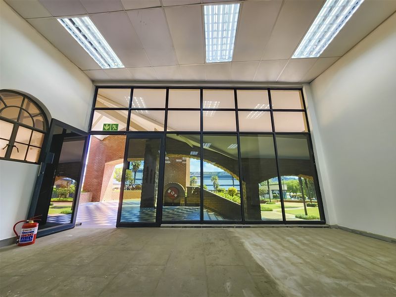 A bright, vacant office space featuring a large glass facade, suspended ceiling with recessed lighting, and an unfinished floor, ready for custom flooring installation.