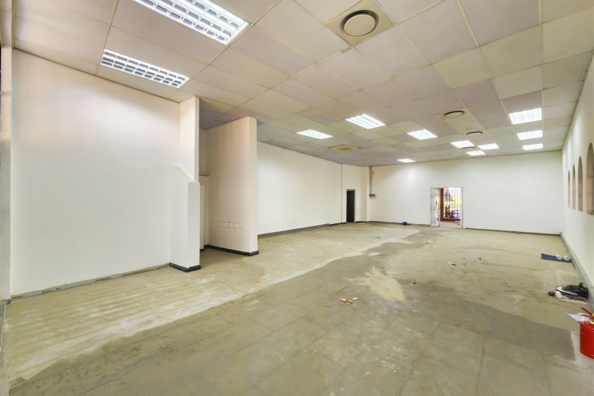 A spacious, vacant office area featuring a suspended ceiling with recessed lighting and unfinished concrete flooring, ready for custom fit-out.