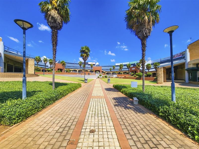 A well-maintained outdoor courtyard area featuring a paved central walkway, landscaped garden beds, and surrounding commercial office building facades.