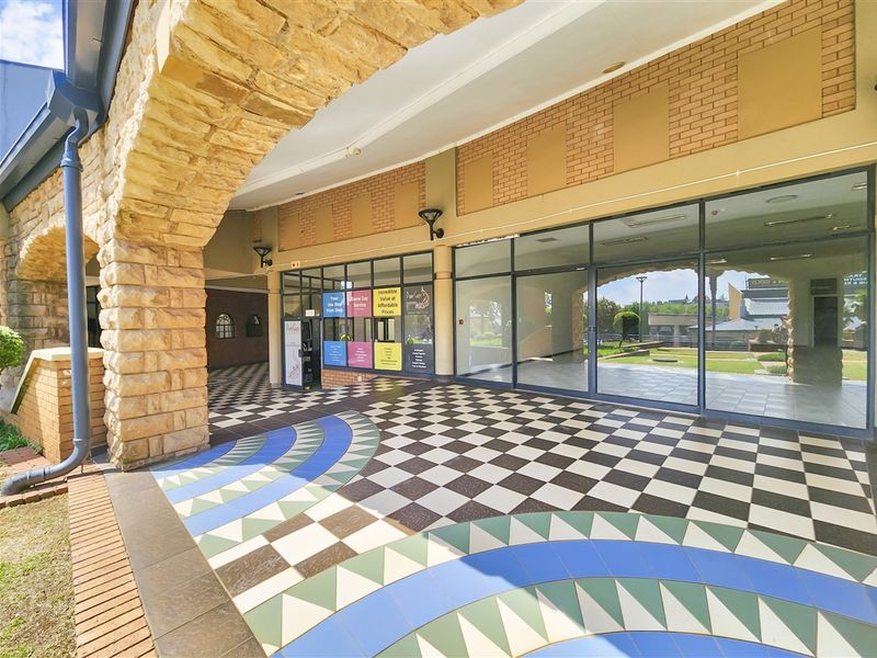 A covered outdoor walkway featuring a decorative stone archway, patterned checkered tile flooring, and large glass storefront windows.