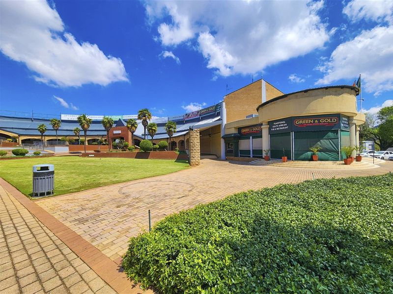 Exterior view of a commercial office and retail complex featuring landscaped gardens, paved walkways, and a prominent corner restaurant entrance.