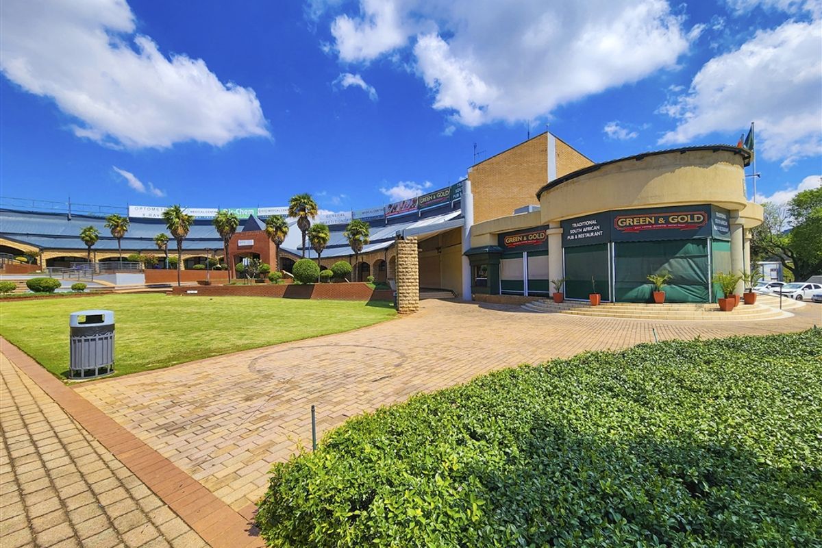 Exterior view of a commercial office and retail complex featuring landscaped gardens, paved walkways, and a prominent corner restaurant entrance.