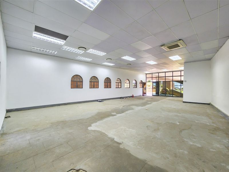 A spacious, vacant office unit featuring a suspended ceiling, recessed lighting, ducted air conditioning, and large glass entrance doors.