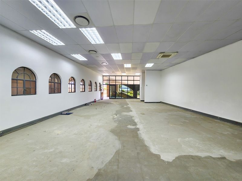 A vacant, open-plan office space featuring arched windows, a suspended ceiling with recessed lighting, and an exposed concrete floor ready for refurbishment.