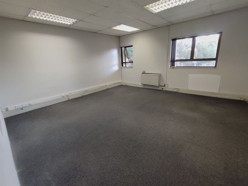 An empty, functional office space featuring a suspended ceiling, recessed lighting, carpeted flooring, and an integrated air conditioning unit.
