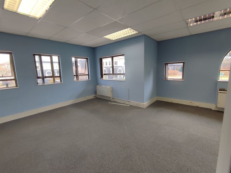 A bright, empty office space featuring carpeted flooring, a suspended ceiling with recessed lighting, and an integrated HVAC unit.