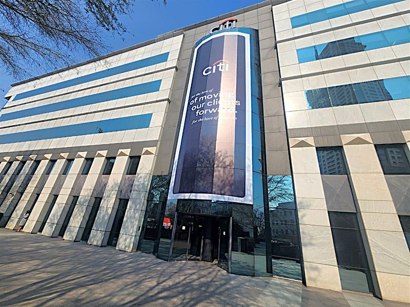 Modern multi-story office building facade featuring stone cladding, extensive glass curtain walling, and prominent corporate branding at the main entrance.