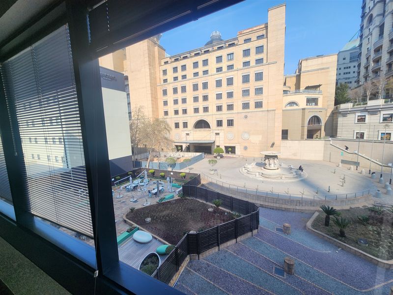 An elevated view from an office window overlooking a paved courtyard with a central fountain and surrounding commercial buildings.