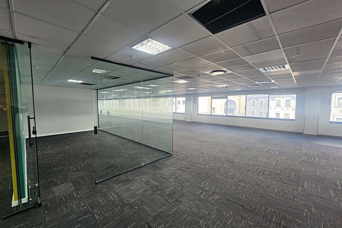 Spacious open-plan office area featuring glass partitioning, carpet tiles, and large windows providing ample natural light.