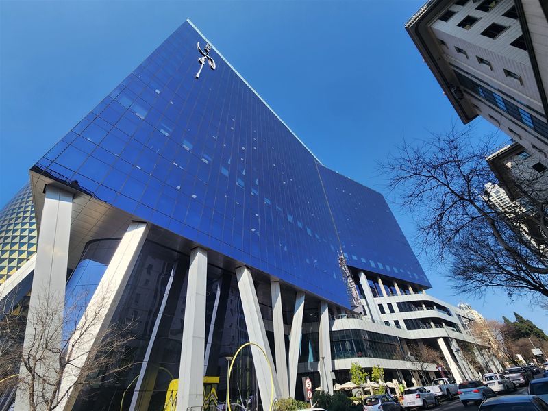 A modern high-rise office building featuring a striking blue glass curtain wall facade and prominent structural support columns.