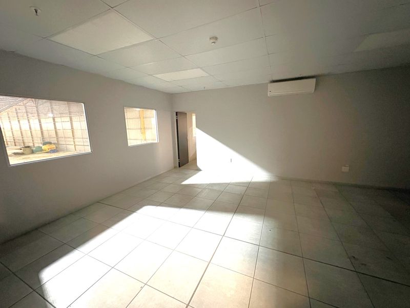 A clean, empty office space featuring tiled flooring, a suspended ceiling, and a wall-mounted air conditioning unit.