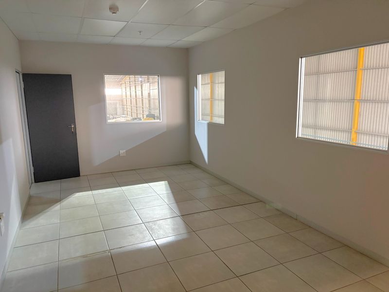 A clean, empty office space featuring tiled flooring, a suspended ceiling, and multiple windows providing natural light, suitable for a professional workspace.
