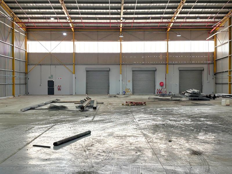 Spacious industrial warehouse unit featuring high ceilings, exposed steel trusses, multiple roller shutter doors, and durable concrete flooring, suitable for various commercial operations.
