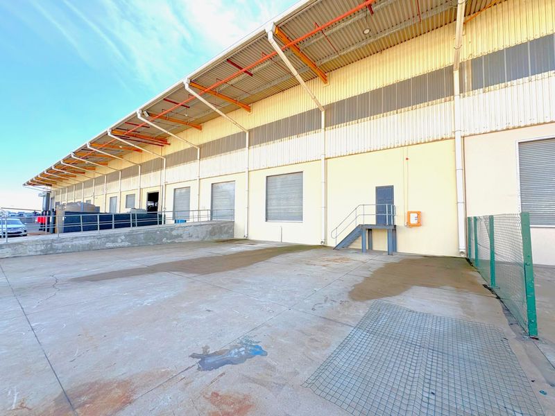 Industrial rear exterior featuring a concrete loading apron, multiple roller shutter doors, metal cladding, and external steel access stairs.