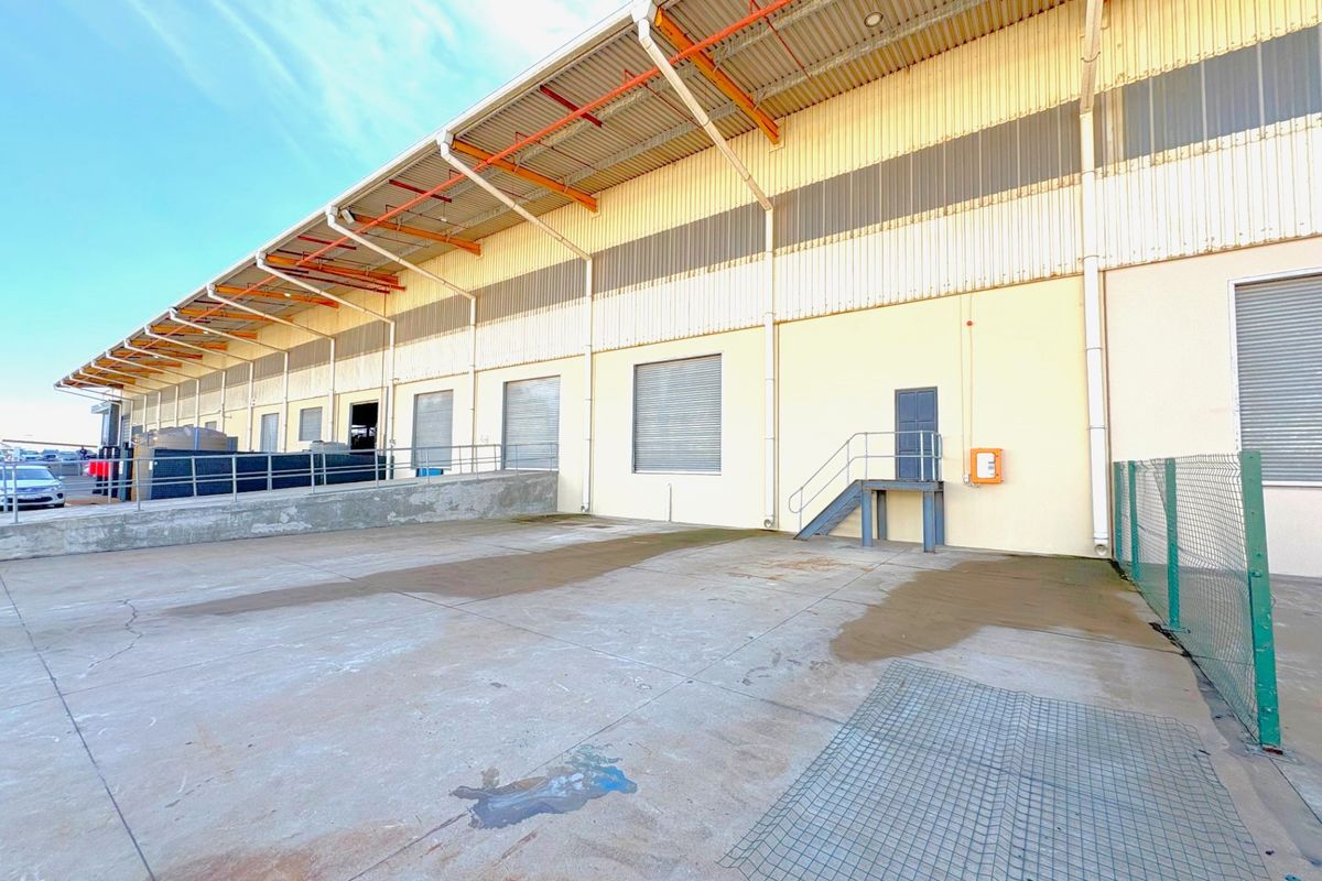 Industrial rear exterior featuring a concrete loading apron, multiple roller shutter doors, metal cladding, and external steel access stairs.