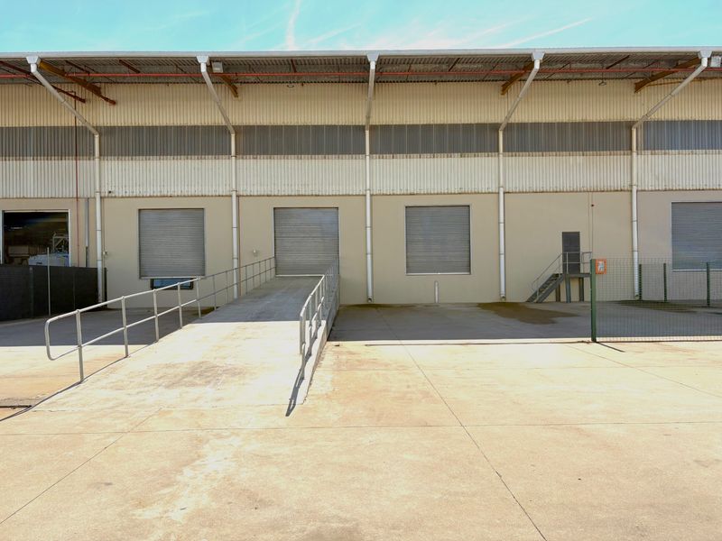 Industrial warehouse exterior featuring multiple roller shutter doors, a concrete loading ramp, and secure perimeter fencing.