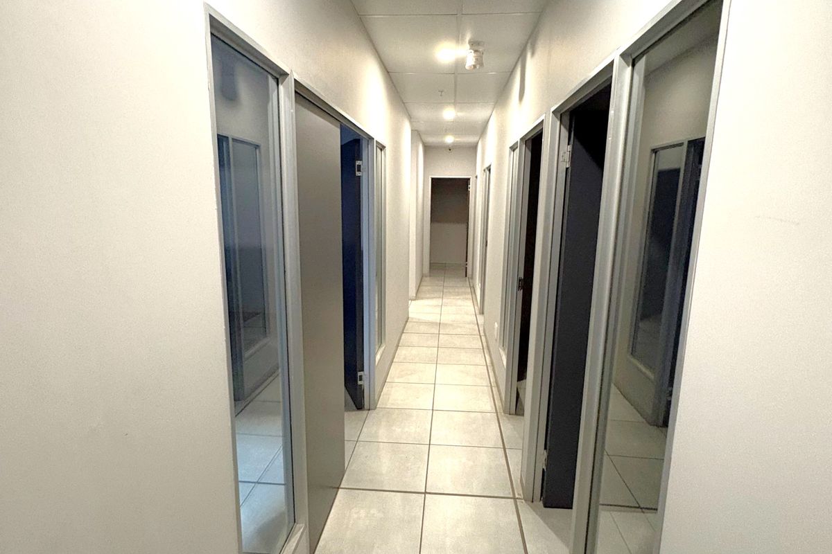 A clean, well-lit industrial hallway featuring tiled flooring, a suspended ceiling with recessed lighting, and multiple glass-panelled office doors.