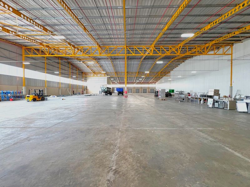 Expansive industrial warehouse space featuring high ceilings with exposed steel trusses, polished concrete flooring, and multiple roller shutter access points.