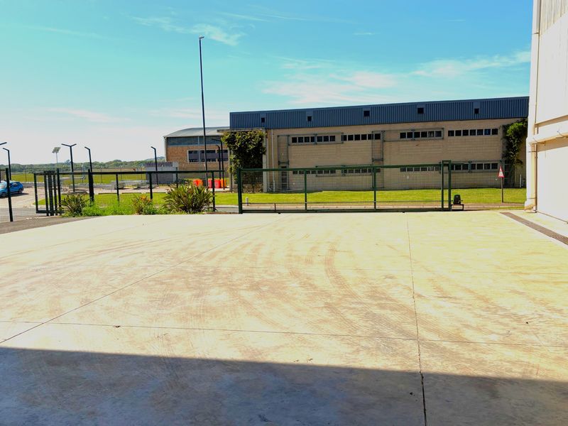 A spacious concrete industrial yard area featuring perimeter fencing, a sliding gate, and a view of the adjacent industrial building facade.