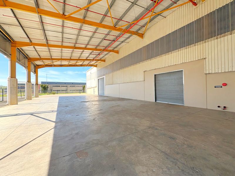 Spacious industrial warehouse area featuring high ceilings, concrete flooring, roller shutter access, and an integrated fire sprinkler system.