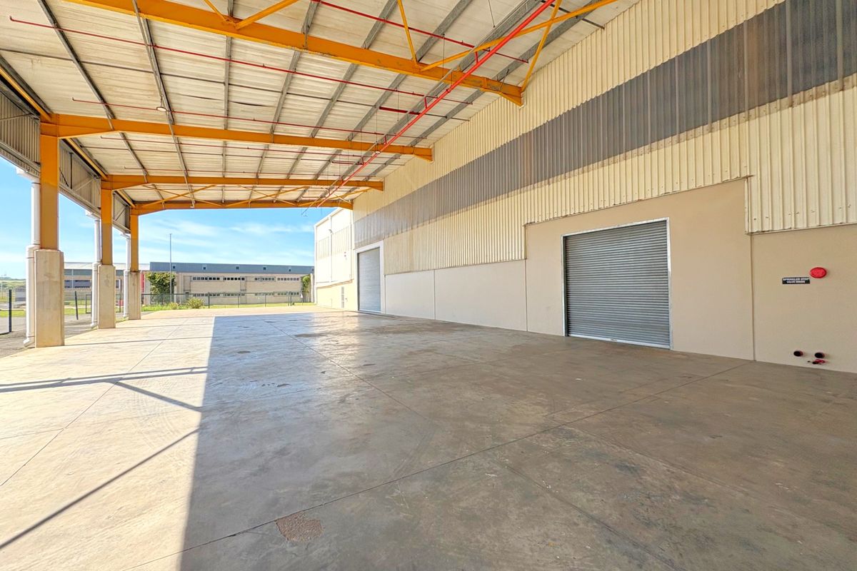 Spacious industrial warehouse area featuring high ceilings, concrete flooring, roller shutter access, and an integrated fire sprinkler system.
