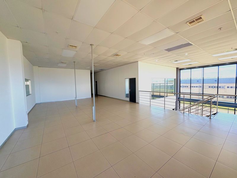 Spacious open-plan industrial office area featuring tiled flooring, a suspended ceiling, and large windows overlooking the exterior.
