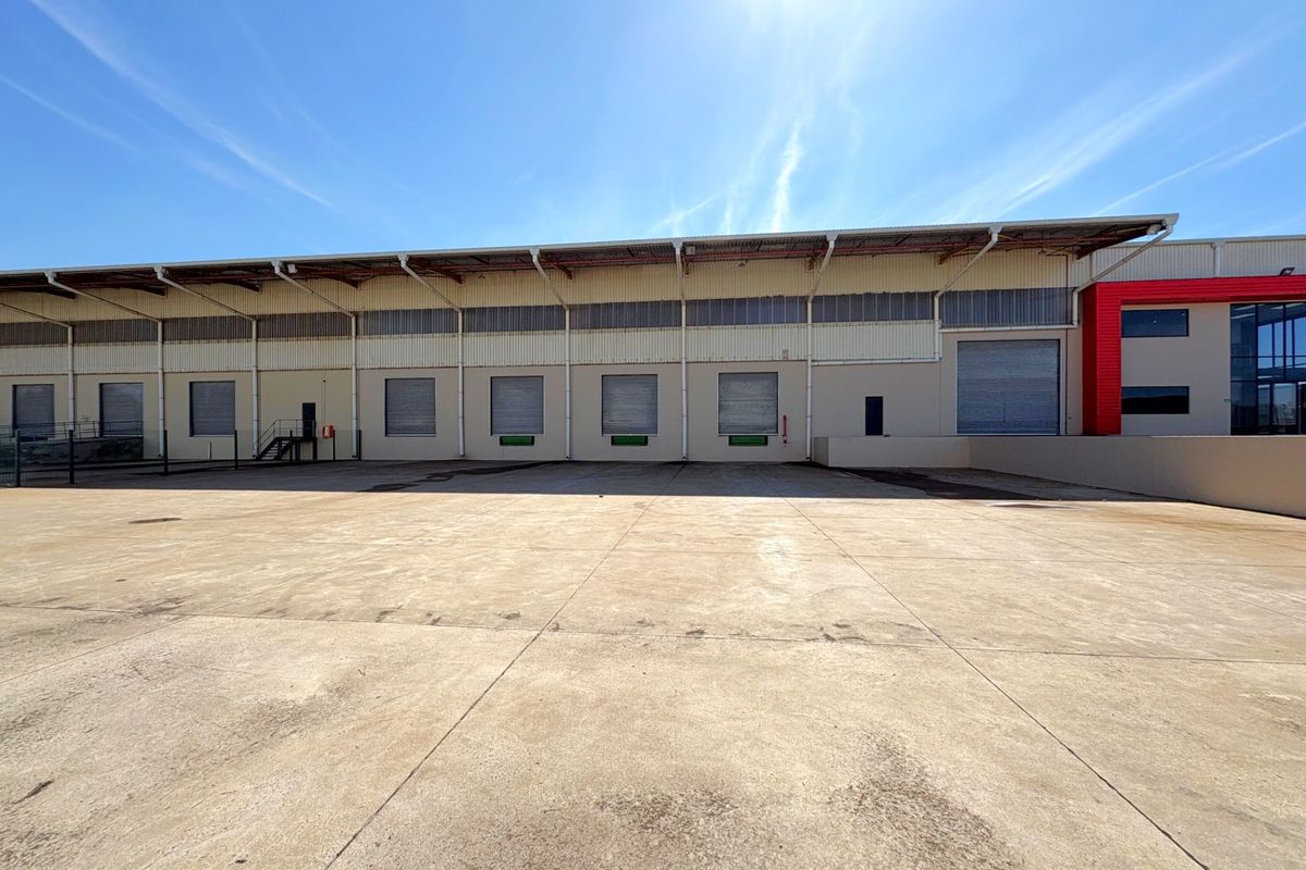 Industrial warehouse exterior featuring multiple roller shutter loading doors and a spacious concrete yard area for logistics and distribution operations.