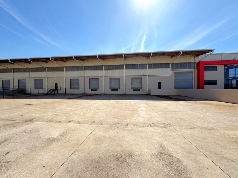 Industrial warehouse exterior featuring multiple roller shutter loading doors and a spacious concrete yard area for logistics and distribution operations.