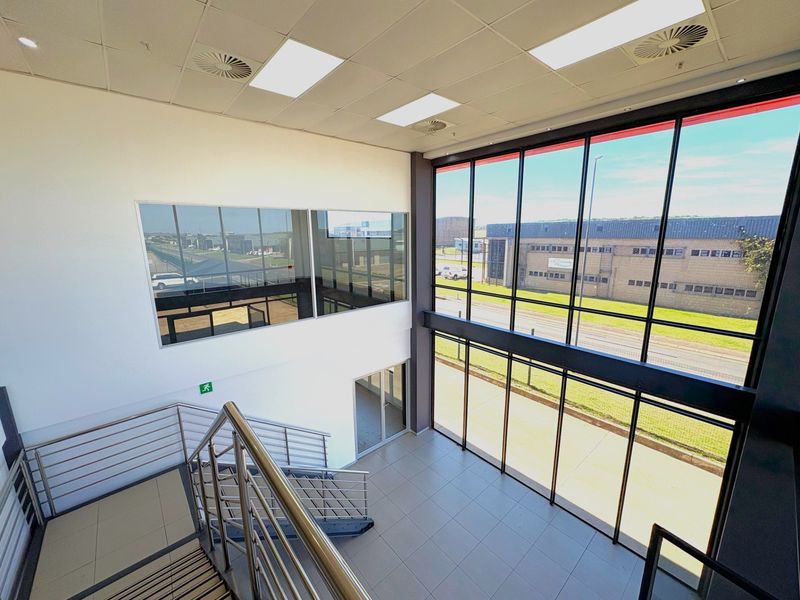 Modern industrial entrance foyer featuring double-volume height, extensive floor-to-ceiling glass windows, tiled flooring, and a contemporary metal staircase with stainless steel railings.