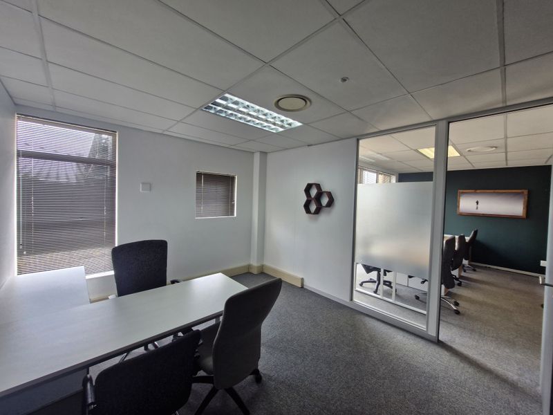 Professional office space featuring a glass partition, suspended ceiling with recessed lighting, carpeted flooring, and large windows with venetian blinds.