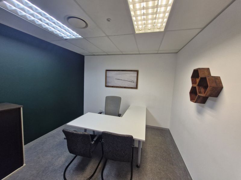 A functional commercial office space featuring a suspended ceiling, recessed lighting, carpeted flooring, and a dark accent wall.