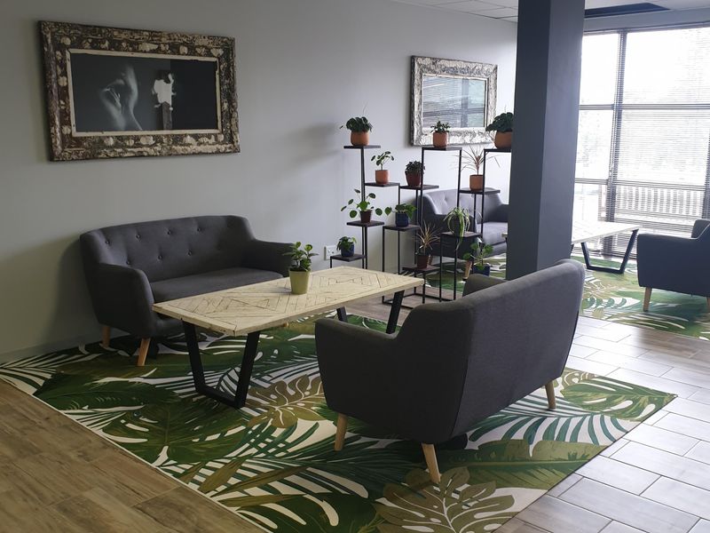 A modern commercial lounge area featuring ceramic tile flooring, a structural column, and large windows providing ample natural light.