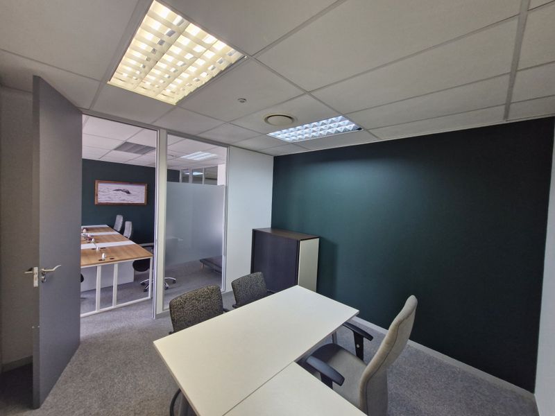 A modern office space featuring a glass partition wall, suspended ceiling with integrated lighting, and dark accent wall, providing a professional work environment.