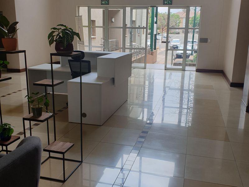 A bright and spacious commercial entrance lobby featuring polished tiled flooring, a built-in reception desk, and large glass doors providing natural light.