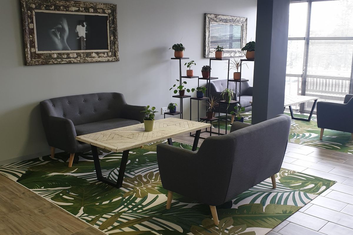 A modern commercial lounge area featuring ceramic tile flooring, a structural column, and large windows providing ample natural light.