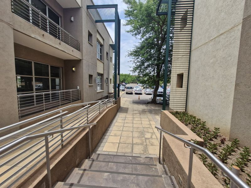 Exterior view of a commercial building featuring a paved walkway, metal railings, and a staircase leading towards a parking area.