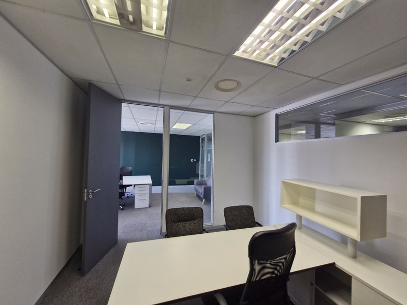 A professional office space featuring a glass partition wall, suspended ceiling with recessed lighting, and built-in shelving, providing a bright and functional workspace.