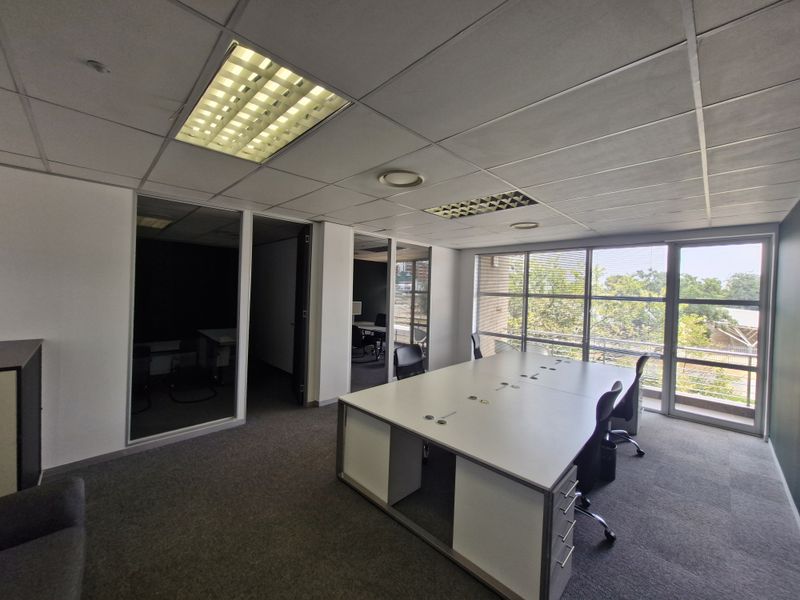 A functional commercial office space featuring glass partitions, suspended ceilings with recessed lighting, and large windows providing natural light.