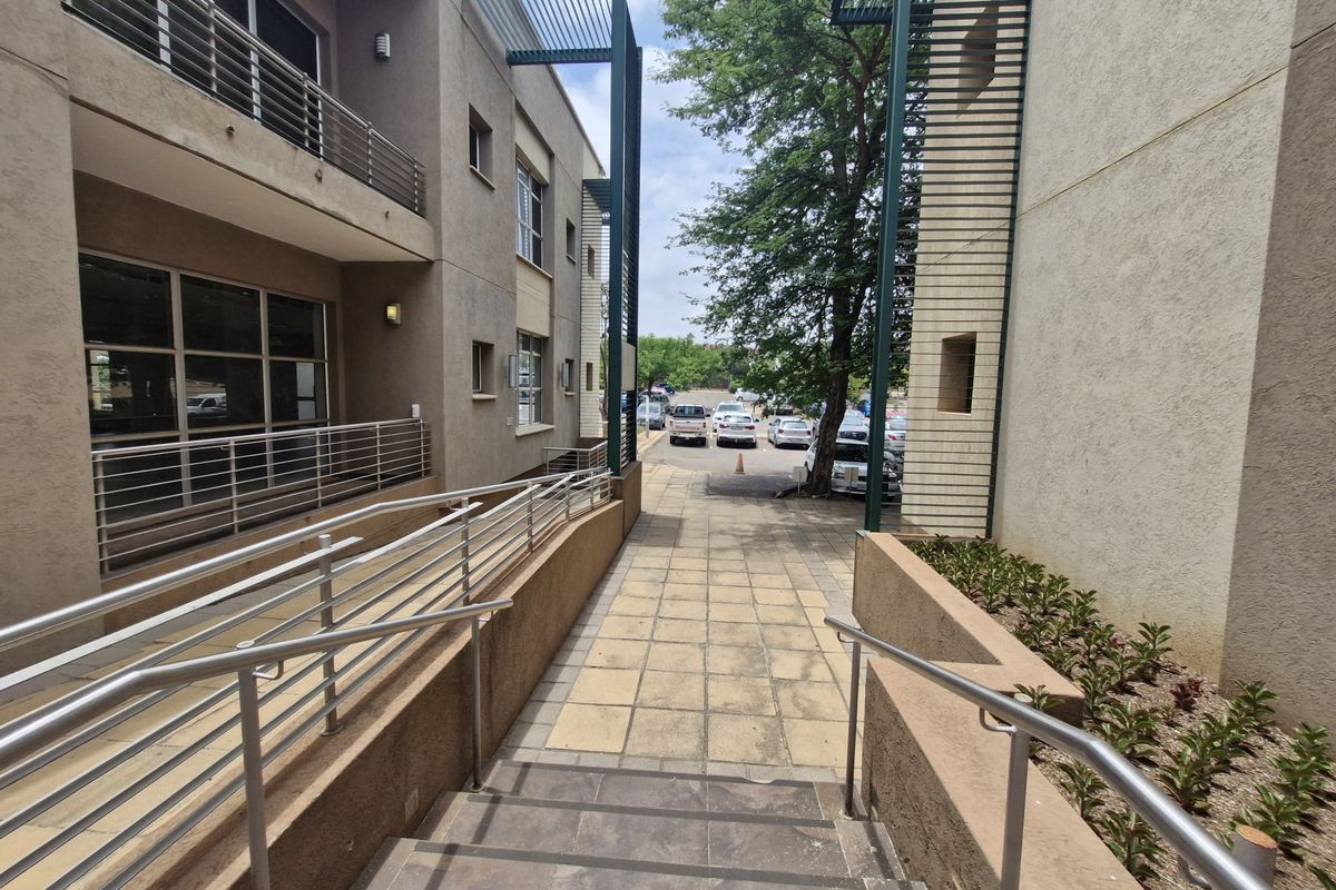 Exterior view of a commercial building featuring a paved walkway, metal railings, and a staircase leading towards a parking area.