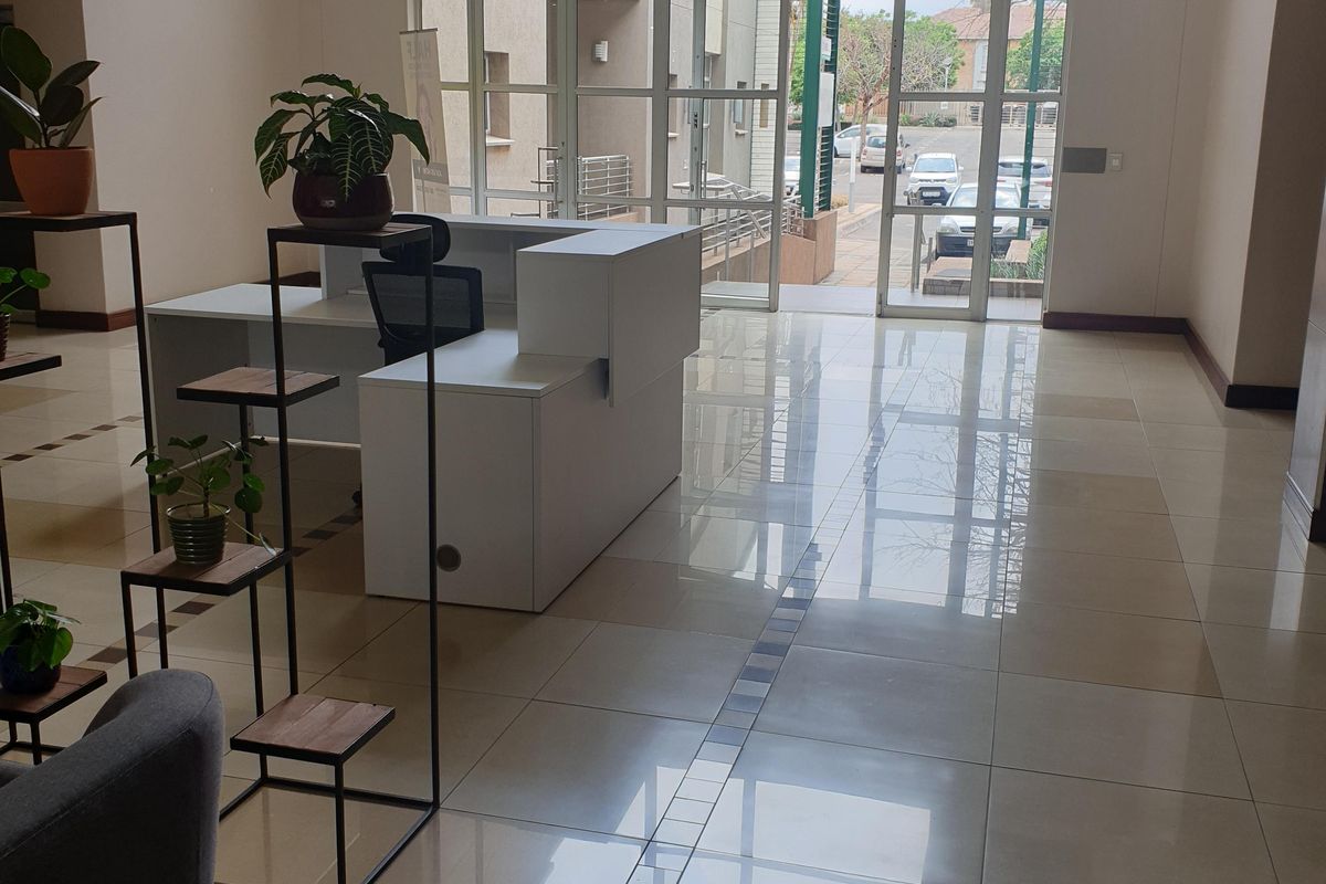 A bright and spacious commercial entrance lobby featuring polished tiled flooring, a built-in reception desk, and large glass doors providing natural light.
