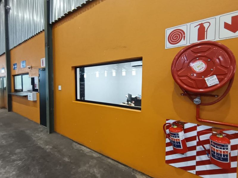 Industrial warehouse interior featuring orange painted walls, concrete flooring, fire safety equipment, and an internal office viewing window.