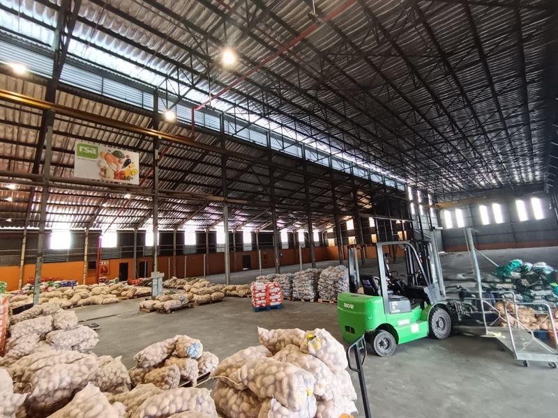 Spacious industrial warehouse featuring high ceilings with exposed steel trusses, concrete flooring, and ample natural light through translucent roof panels.