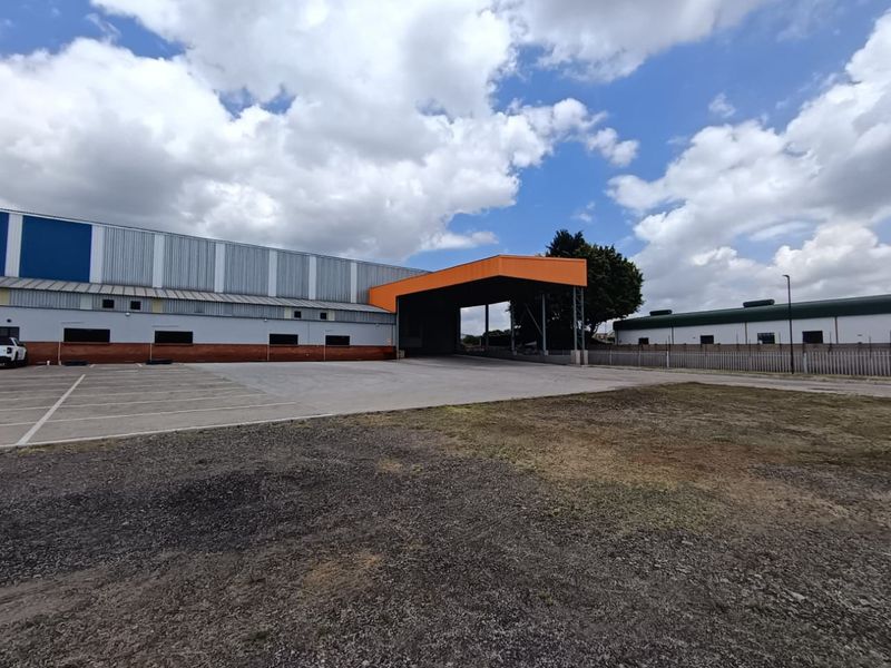 Industrial property exterior featuring a large concrete loading bay, steel canopy, and ample asphalt parking space within a fenced perimeter.