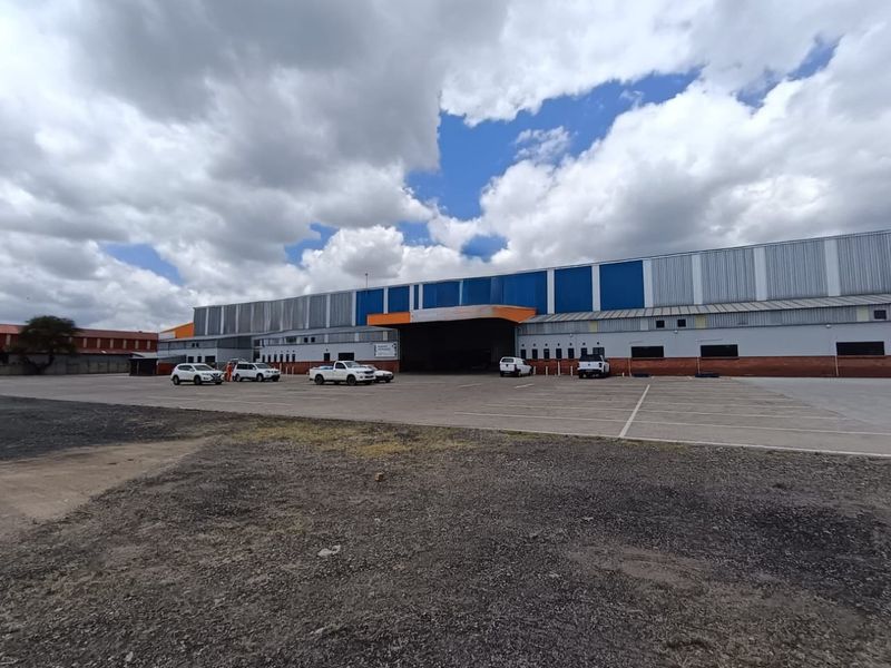 Large industrial warehouse facility featuring a spacious asphalt parking area and a prominent covered loading bay entrance.