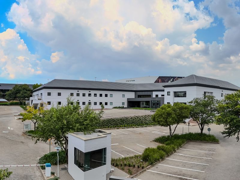 Wide-angle view of an industrial property featuring a large paved parking area, covered parking bays, a security guard house, and well-maintained landscaping.