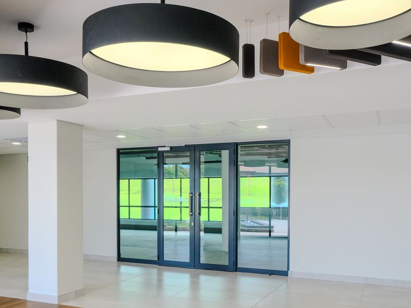 Modern entrance area featuring tiled flooring, large contemporary pendant lighting, acoustic ceiling panels, and expansive aluminium-framed glass doors leading to the exterior.