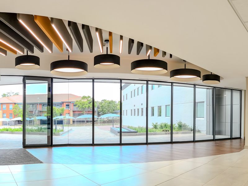 Modern, spacious industrial hallway featuring floor-to-ceiling glass walls, decorative suspended ceiling baffles, and high-quality tiled flooring with excellent natural light.