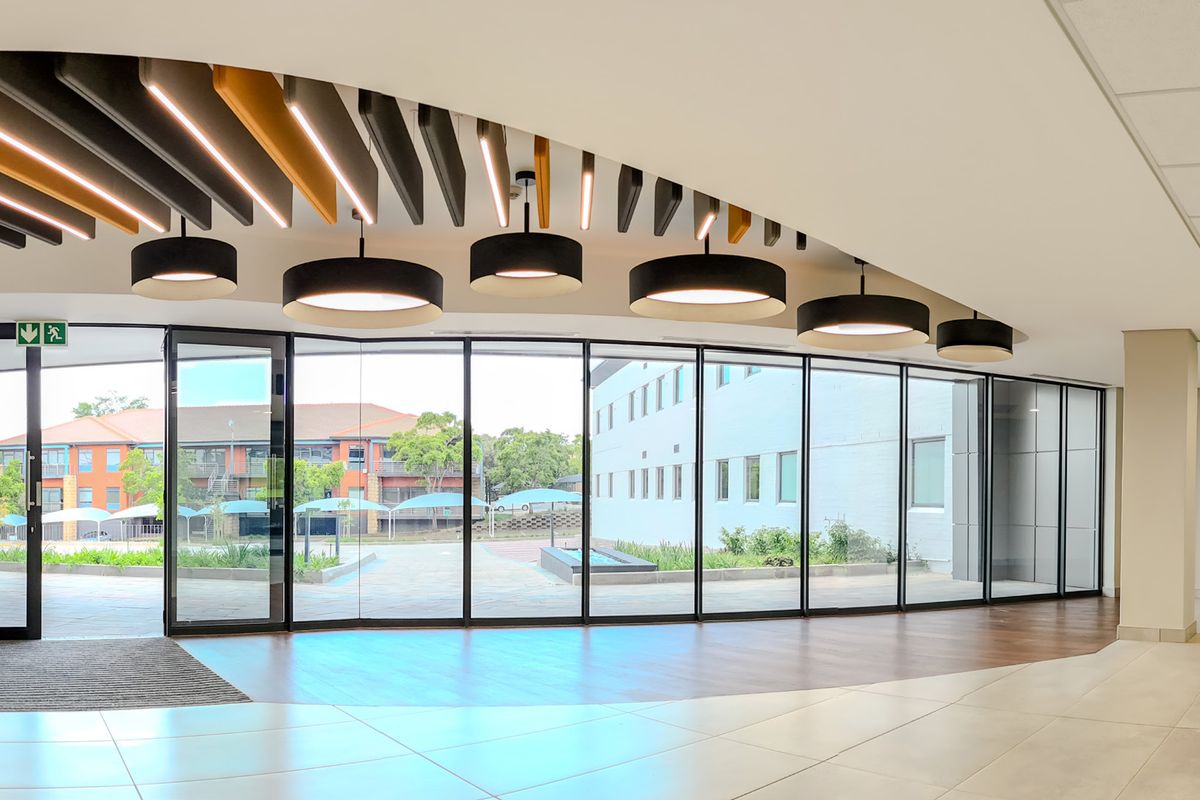 Modern, spacious industrial hallway featuring floor-to-ceiling glass walls, decorative suspended ceiling baffles, and high-quality tiled flooring with excellent natural light.