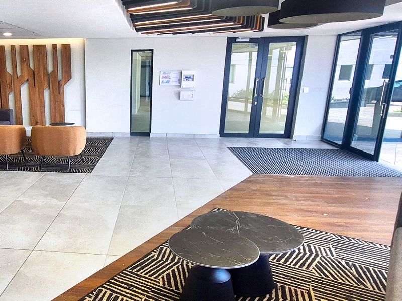 Modern industrial office building entrance lobby featuring large glass doors, tiled flooring, and decorative timber wall paneling.