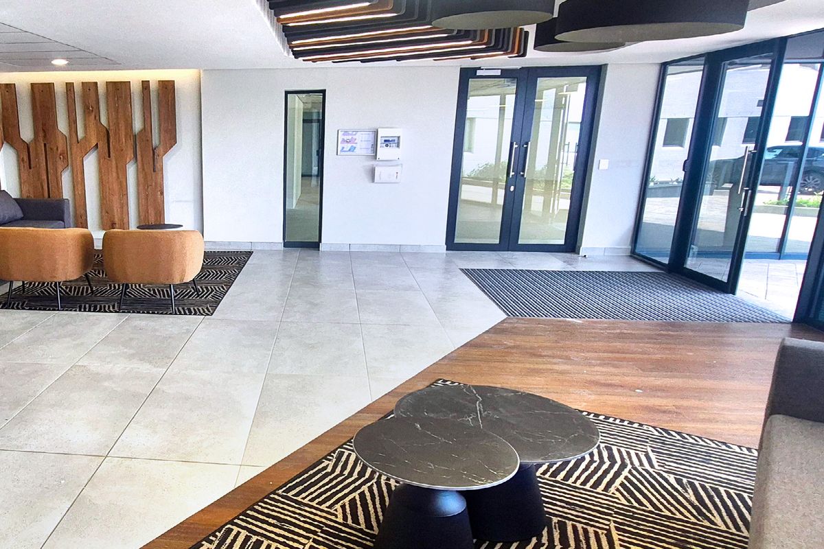Modern industrial office building entrance lobby featuring large glass doors, tiled flooring, and decorative timber wall paneling.